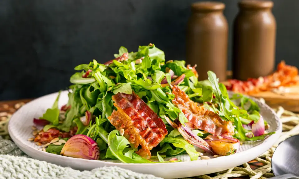 Salat mit Rucola, roten Zwiebeln und knusprigem Speck. Perfekte warme Beilagen zum Salat, die für zusätzlichen Geschmack sorgen.