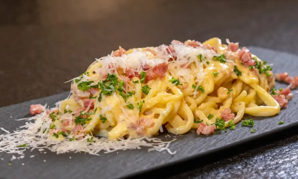 Ein Teller cremiger Spaghetti Carbonara, garniert mit Speckwürfeln, Petersilie und frisch geriebenem Parmesan.