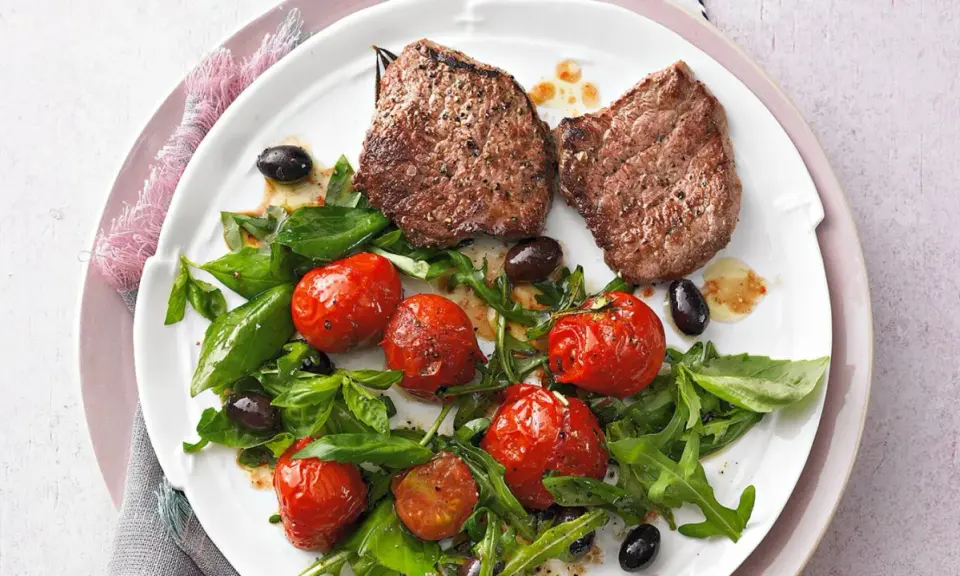 Zwei saftige Minutensteaks im Backofen zubereitet, serviert mit gerösteten Kirschtomaten, Rucola und schwarzen Oliven.