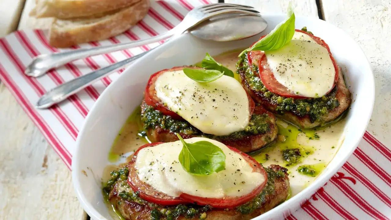 Saftige schweine minutensteaks im backofen, belegt mit Tomate, Mozzarella und Pesto, garniert mit Basilikum.