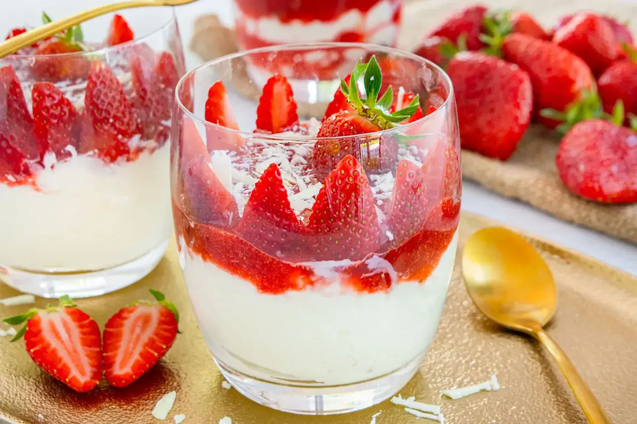 Erdbeer-Mascarpone-Creme in Gläsern, garniert mit frischen Erdbeeren und weißer Schokolade. Ein Löffel liegt daneben.