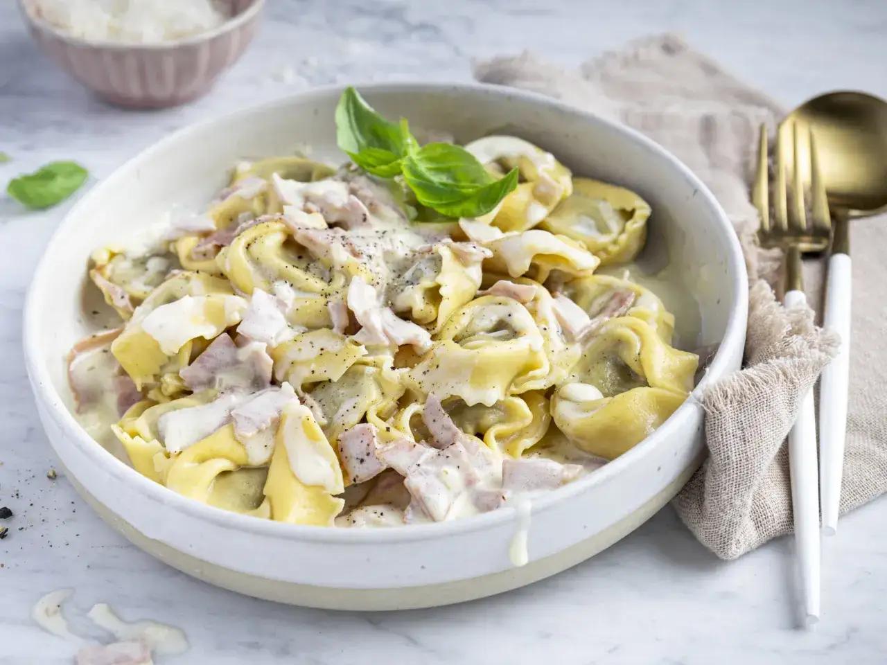 Ein Teller mit Tortellini alla panna, garniert mit Basilikum und bestreut mit schwarzem Pfeffer. Cremige Sauce umh&uuml;llt die gef&uuml;llten Teigtaschen.