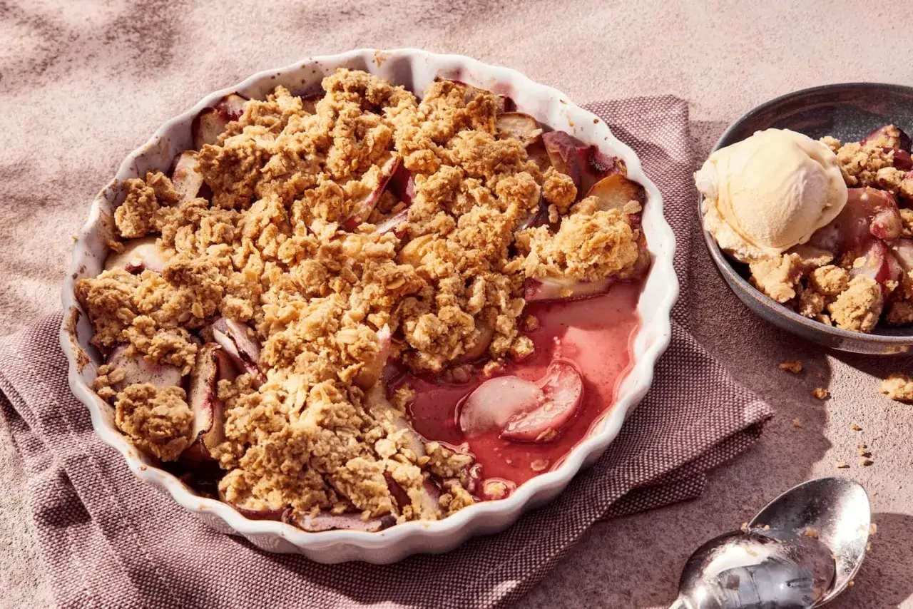 Ein warmer Pfirsich Crumble mit knuspriger Streuseldecke und einer Kugel Vanilleeis daneben.