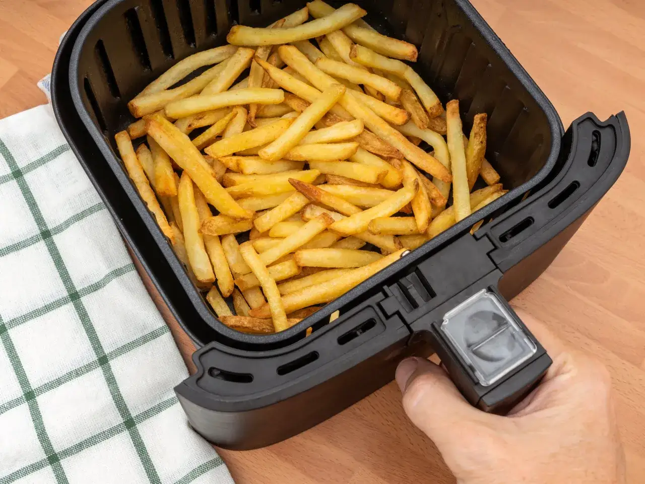 Goldbraune Pommes liegen in einem Airfryer-Korb. Perfekt f&uuml;r einen schnellen Snack!
