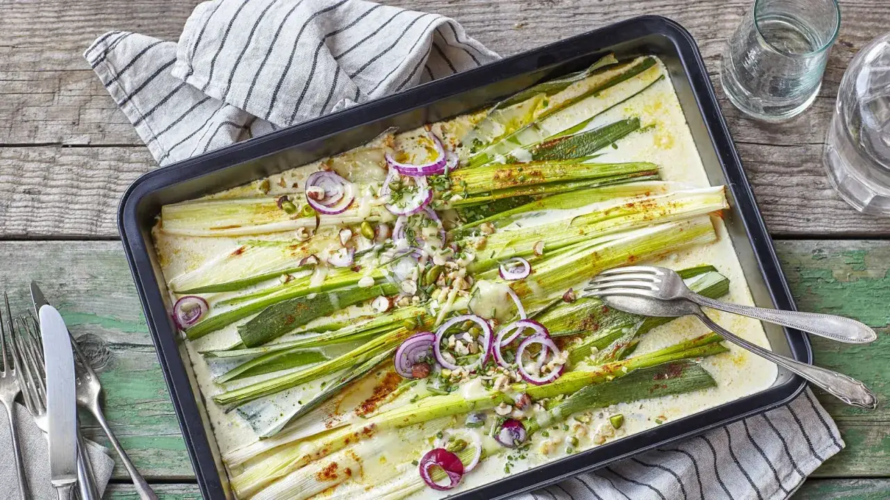 Ofen-Lauch-Rezepte: Lauch in cremiger Sauce mit roten Zwiebeln und Nüssen, bereit zum Servieren.