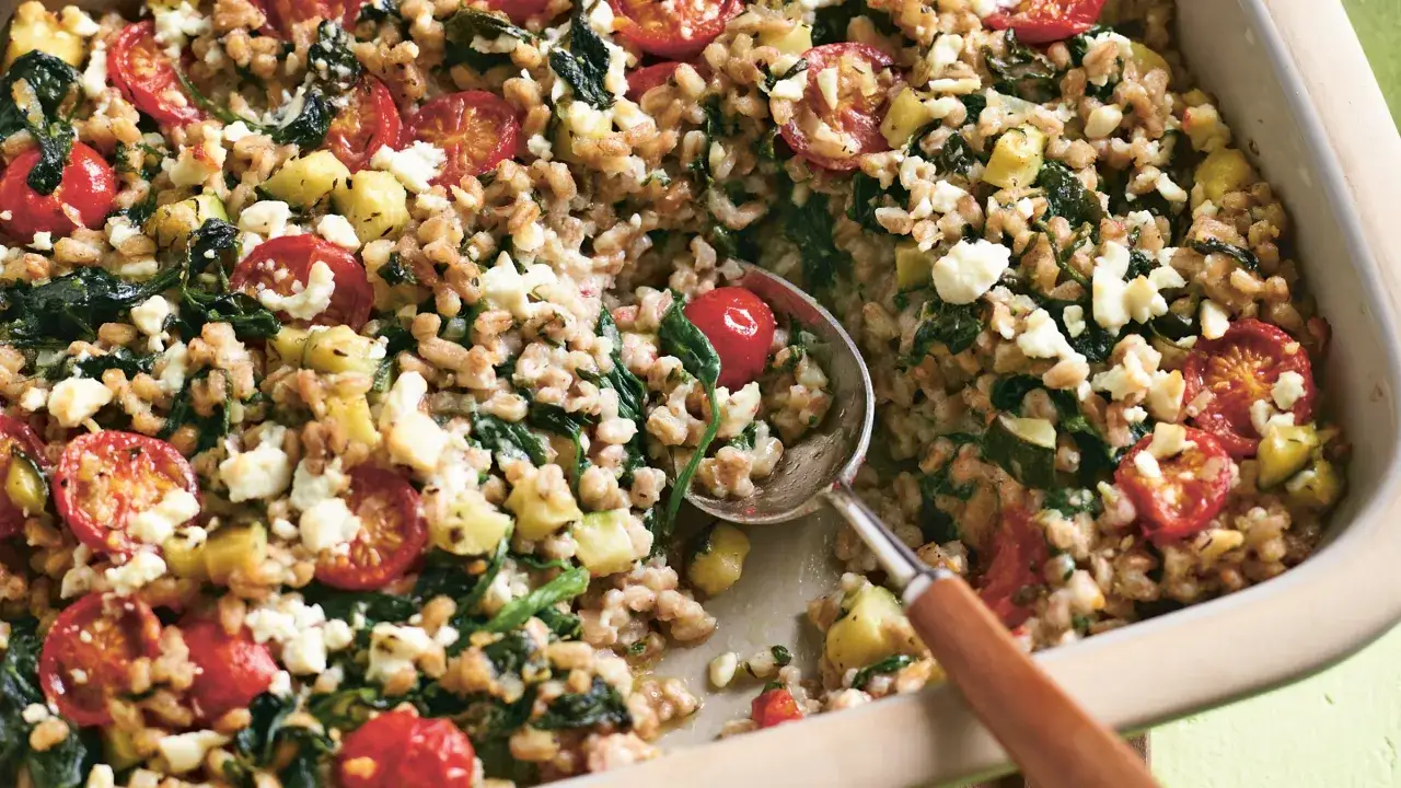 Dinkel kochen: Ein Auflauf mit Dinkel, Kirschtomaten, Zucchini und Feta. Eine L&ouml;ffelprobe zeigt die k&ouml;stliche Mischung.