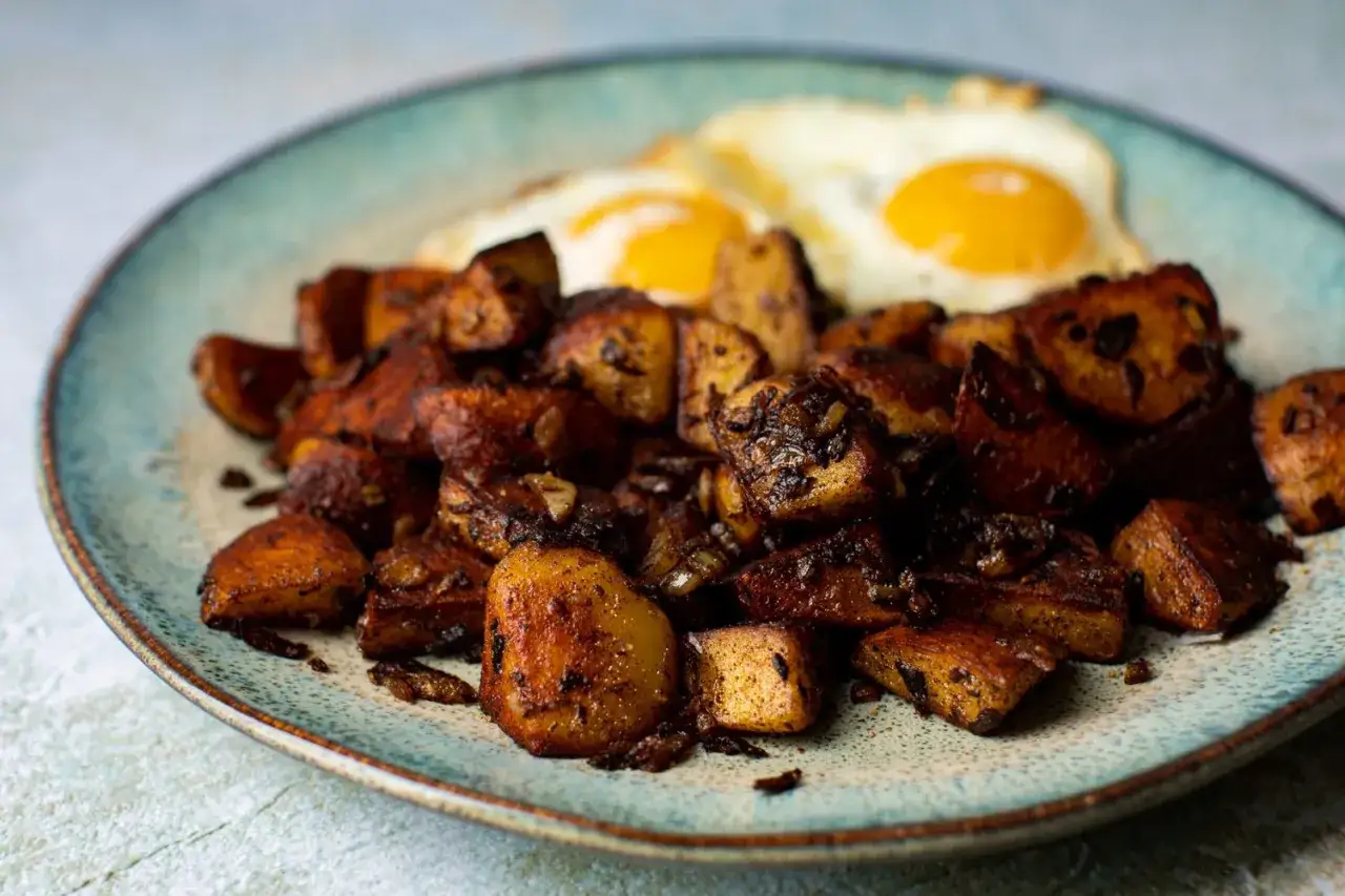 Herzhafte bratkartoffeln mit mehligen Kartoffeln, goldbraun gebraten, serviert mit zwei Spiegeleiern auf einem blauen Teller.