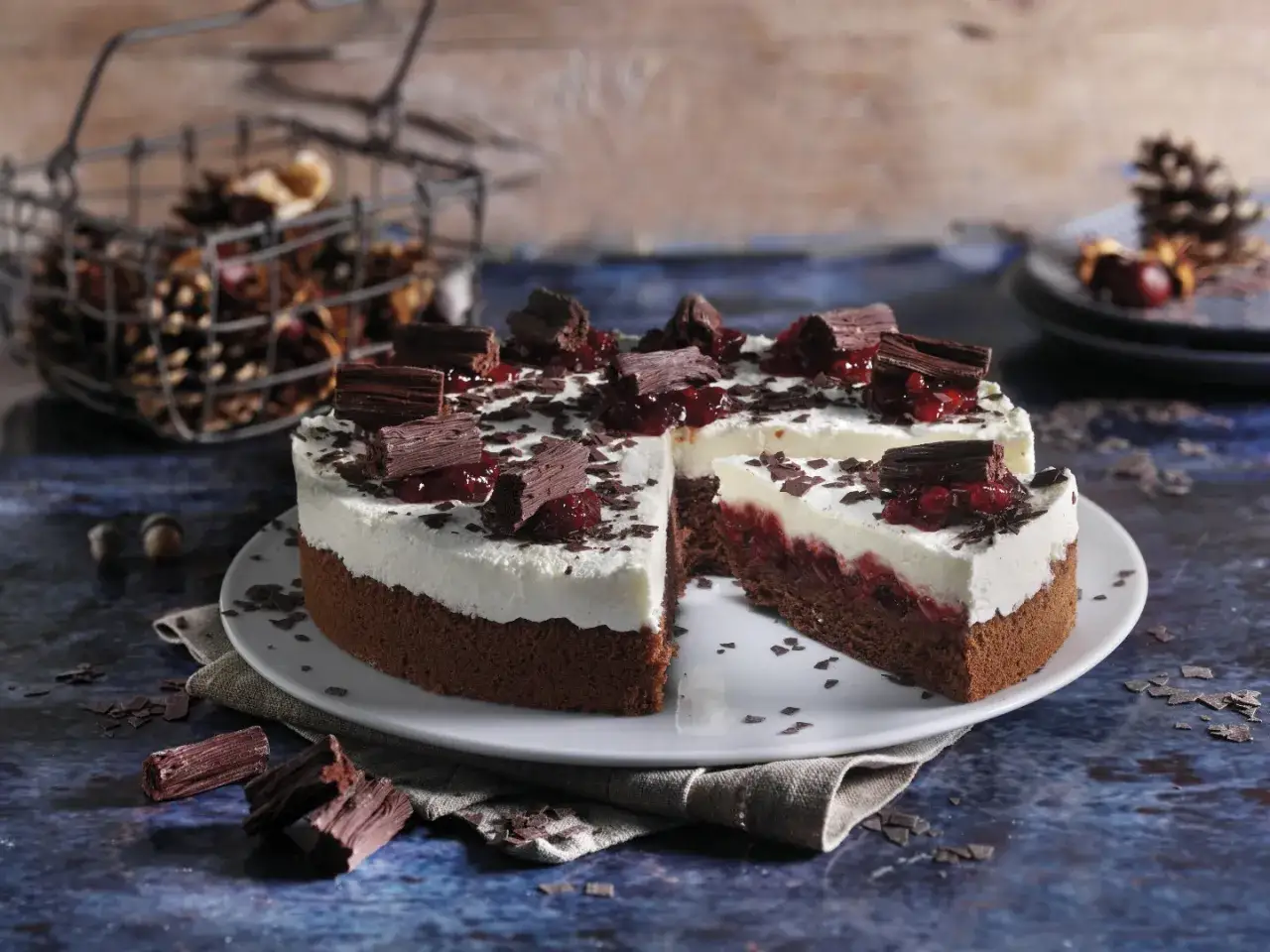 Schokoladen-Sahne-Torte mit Preiselbeeren und Schokost&uuml;ckchen, dekoriert mit Schokoraspeln. Ein St&uuml;ck ist herausgeschnitten.
