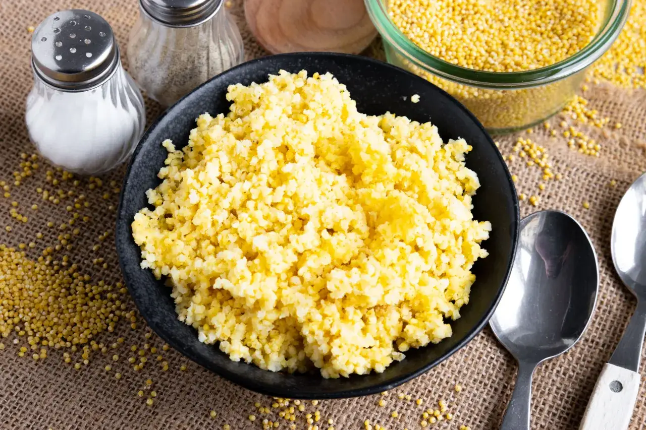 Fertig gekochte Goldhirse in einer schwarzen Sch&uuml;ssel, bereit zum Servieren. Daneben stehen Salz- und Pfefferstreuer sowie L&ouml;ffel.