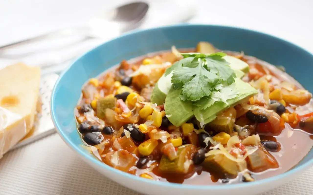Herzhaftes Chili sin Carne mit schwarzen Bohnen, Mais, Zucchini und Avocado-Topping.
