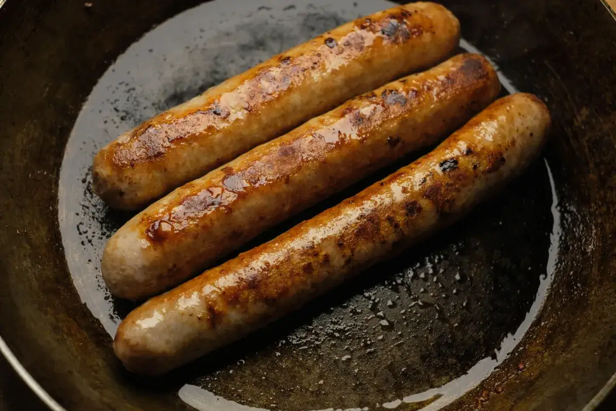 Drei goldbraune Bratw&uuml;rste brutzeln in einer Pfanne. Perfekt f&uuml;r leckere Bratwurst Rezepte!