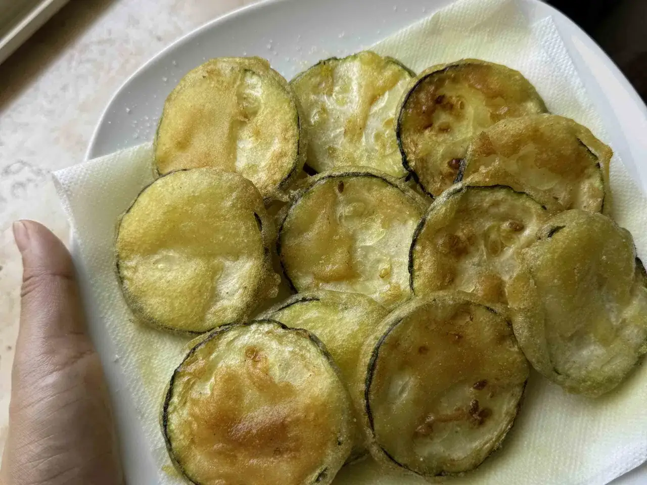 Zucchini gebraten italienisch: goldbraune, knusprige Scheiben auf K&uuml;chenpapier, bereit zum Genie&szlig;en.
