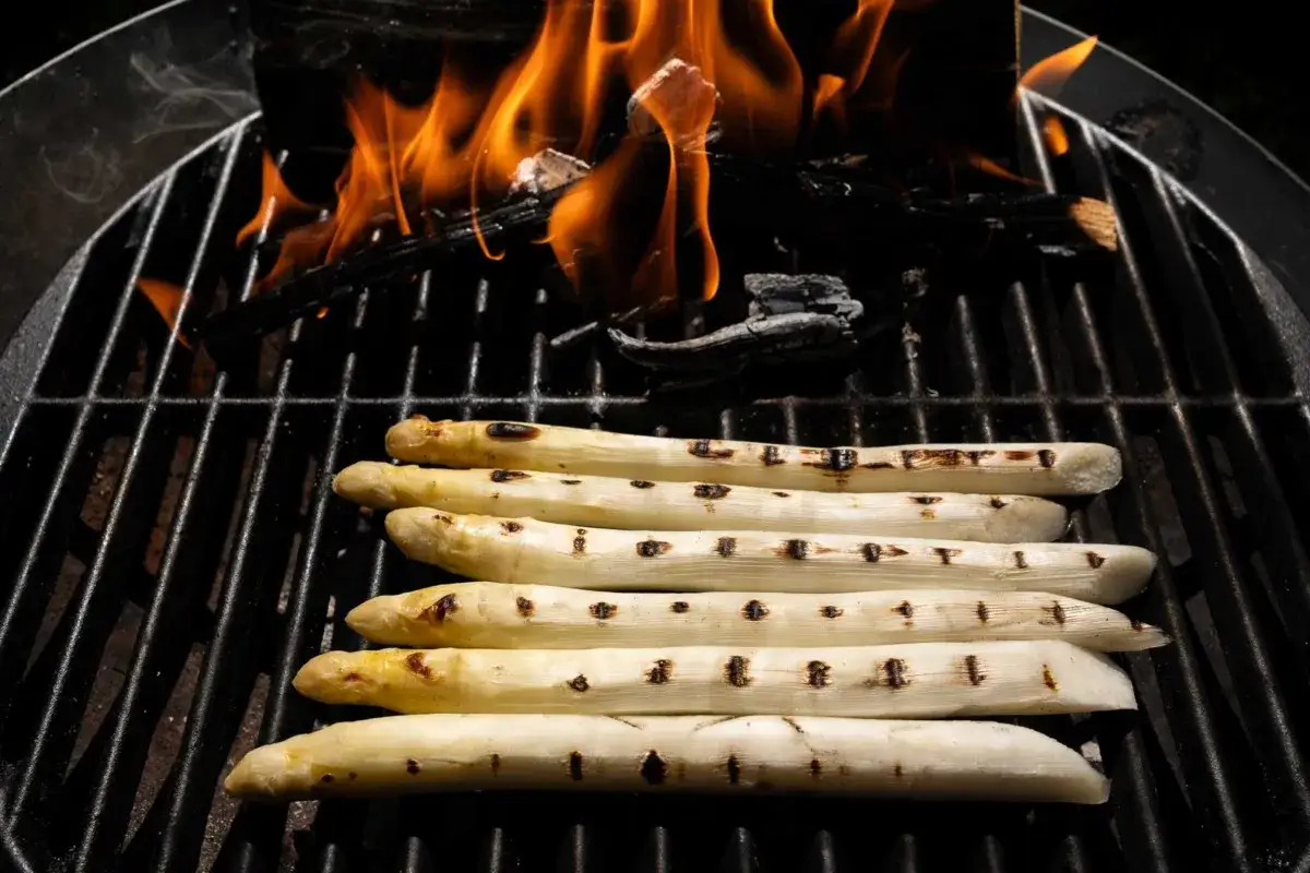 Wei&szlig;e Spargelstangen garen auf einem Grill &uuml;ber lodernden Flammen. Die Grillstreifen zeichnen sich auf dem Spargel ab.