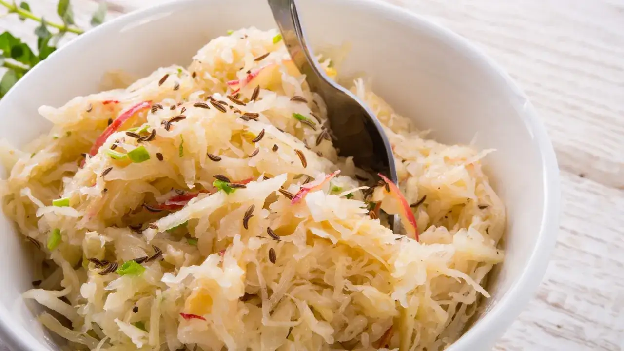 Hausgemachtes Sauerkraut nach Hausfrauenart, verfeinert mit Kümmel und Apfelstücken, serviert in einer weißen Schüssel.