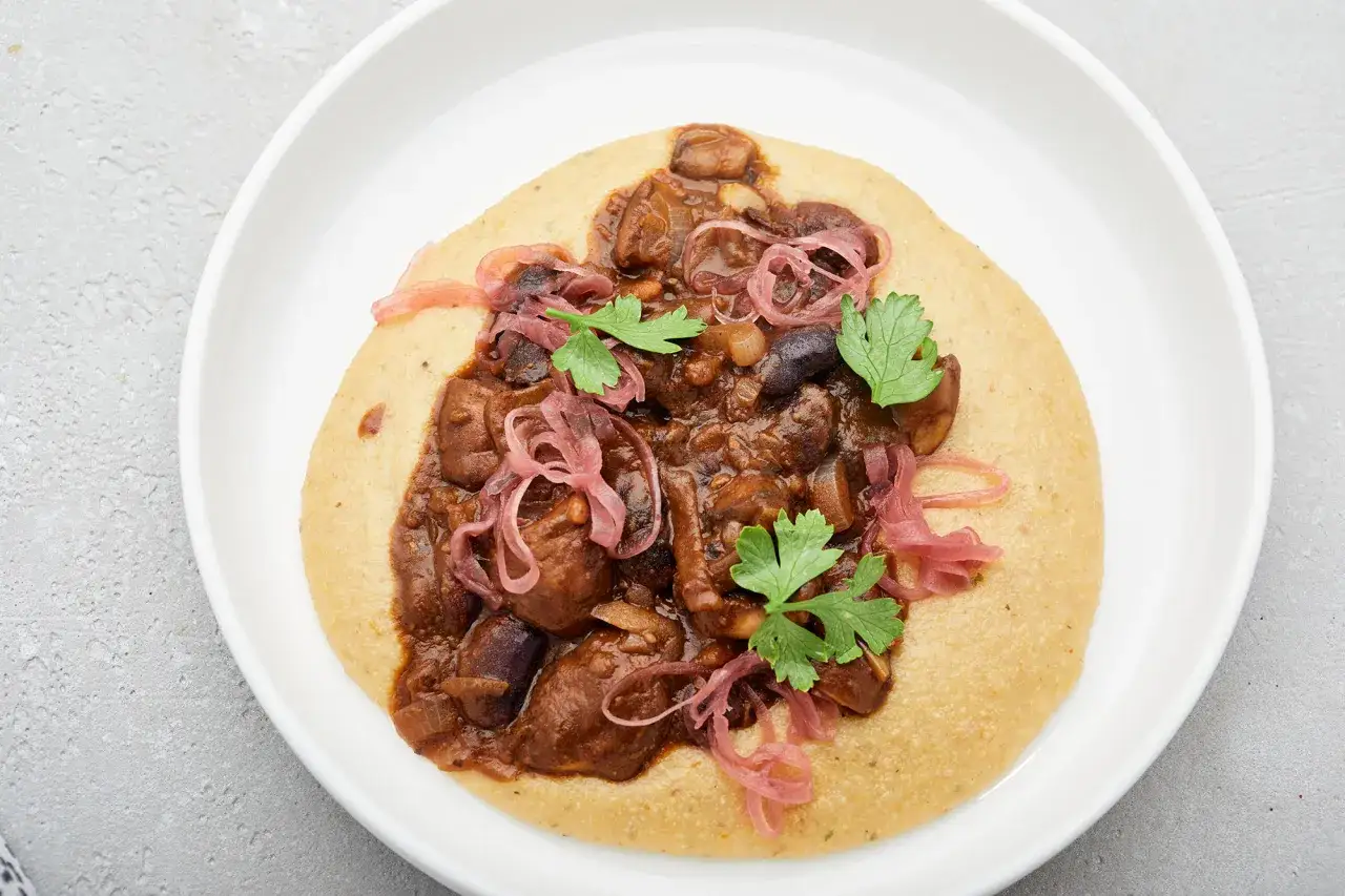 Herzhaftes Pilzragout auf cremiger Polenta, garniert mit eingelegten roten Zwiebeln und Petersilie. So ist Polenta genau richtig!