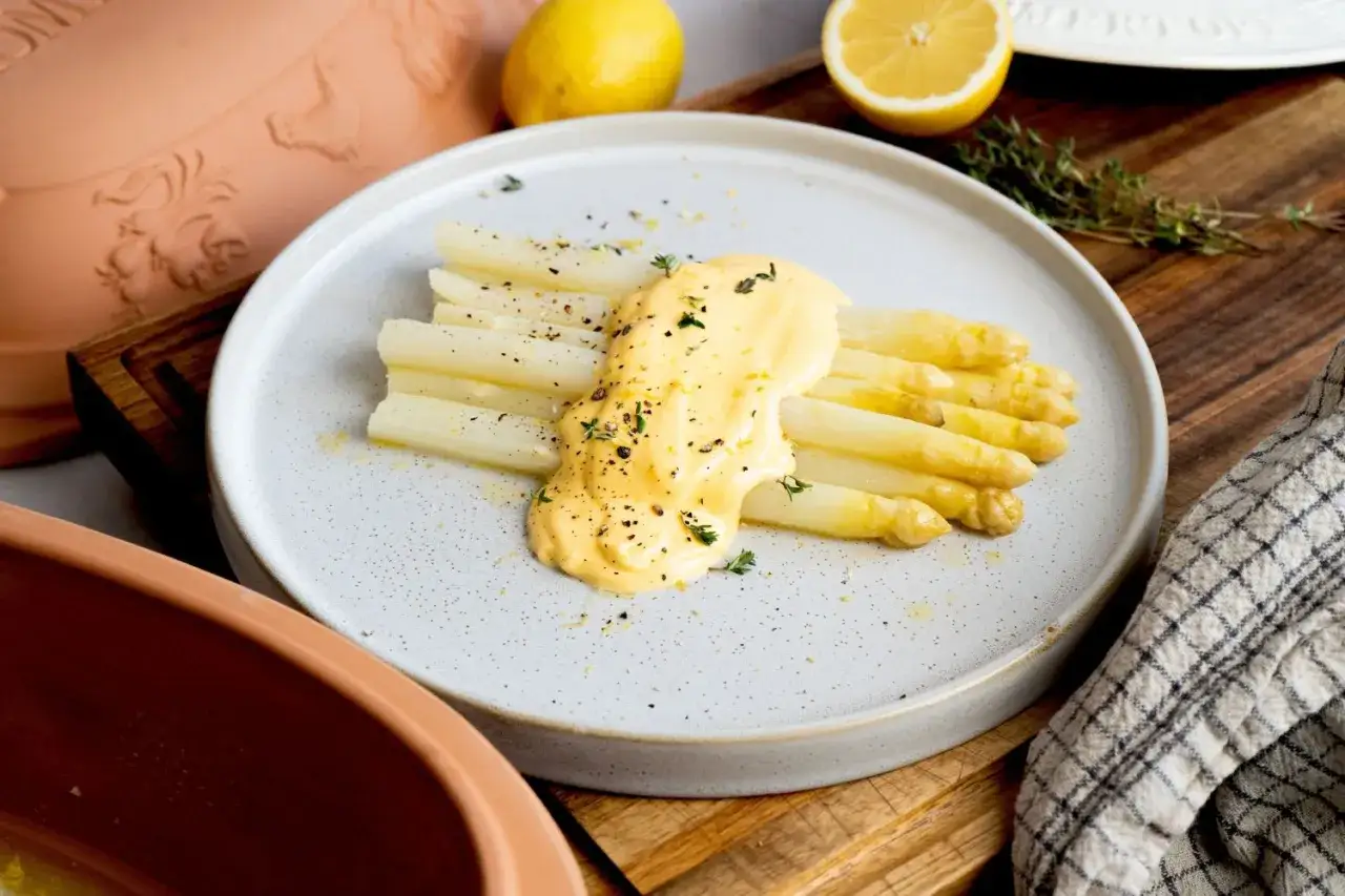 Frischer weißer Spargel mit cremiger Hollandaise, garniert mit Kräutern und Pfeffer. Ein Klassiker, der auf der Zunge zergeht.