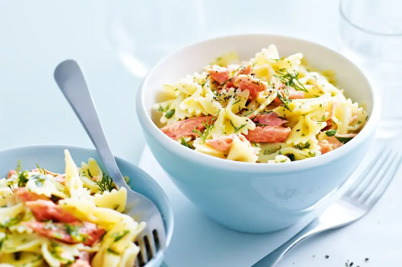 Zwei Sch&uuml;sseln mit Farfalle-Nudeln, verfeinert mit Lachs und Dill. Ein L&ouml;ffel in der linken Sch&uuml;ssel, eine Gabel daneben.