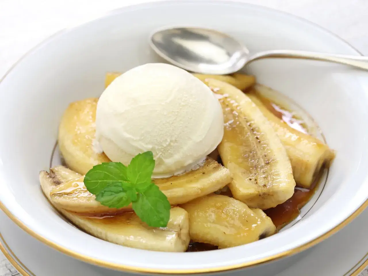 Gebackene Banane mit einer Kugel Vanilleeis, garniert mit Minze, in einer wei&szlig;en Sch&uuml;ssel mit goldenem Rand.
