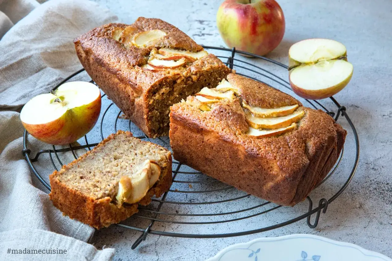 Saftiger Apfelkuchen mit Apfelmus-Note, garniert mit frischen Apfelscheiben. Ein St&uuml;ck ist bereits angeschnitten.