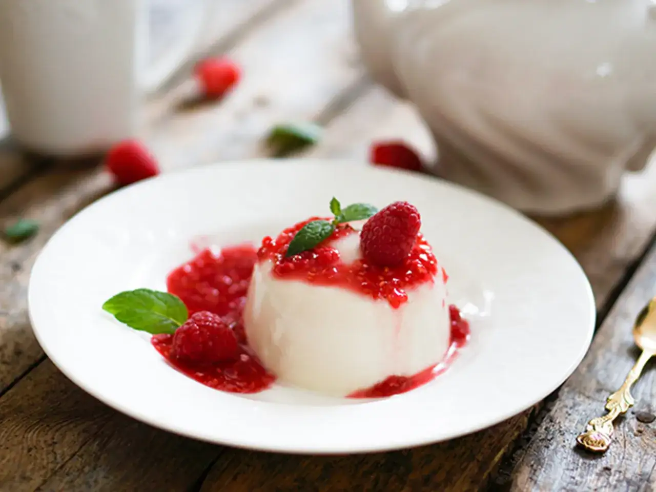 Cremige Panna cotta mit Himbeersauce und frischen Himbeeren, garniert mit Minze. Ein süßer Genuss!