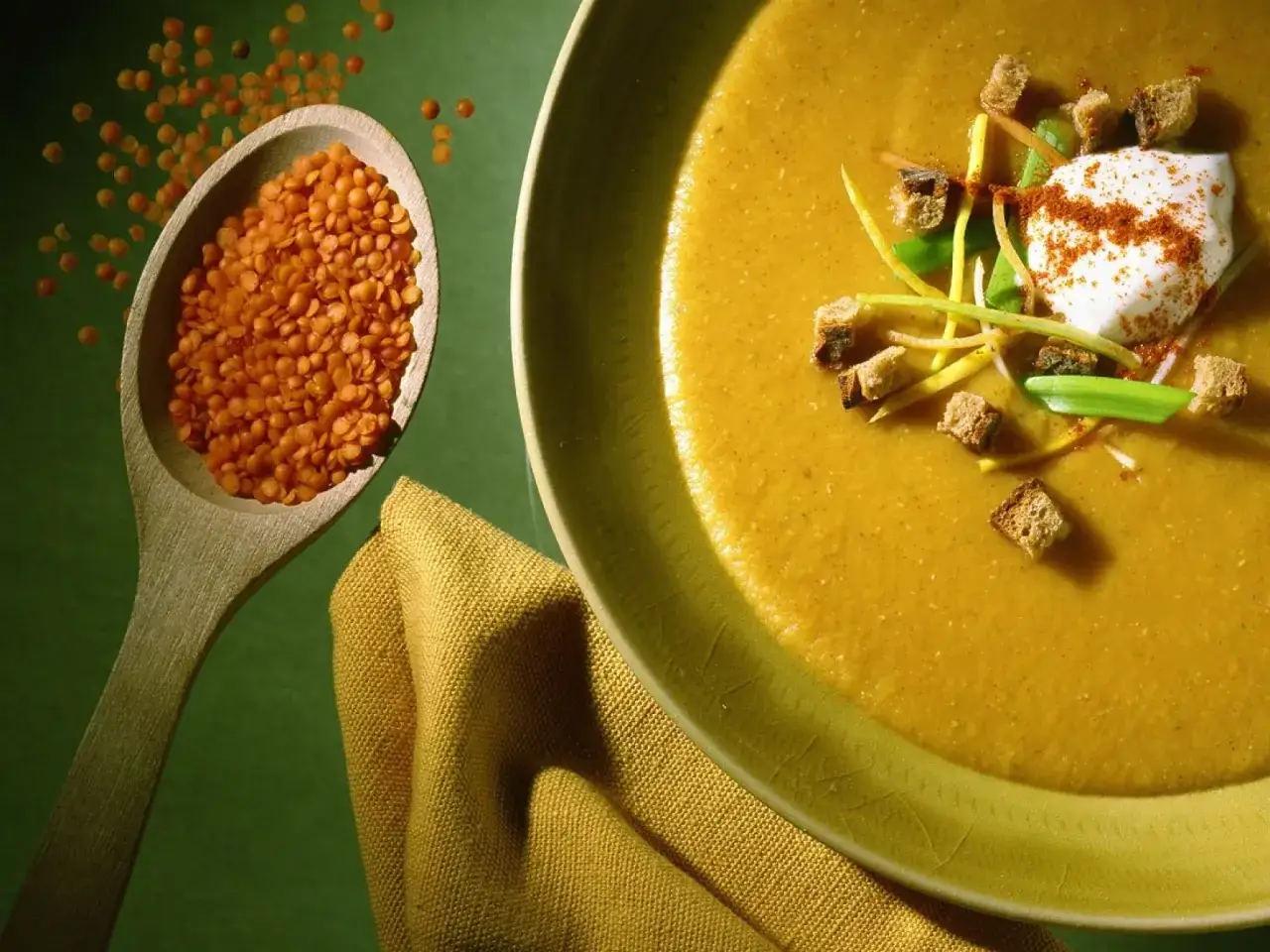 Eine cremige Linsensuppe, garniert mit Croutons und einem Klecks Sauerrahm. Daneben ein Holzlöffel voller roter Linsen, bereit für köstliche Linsen Rezepte.