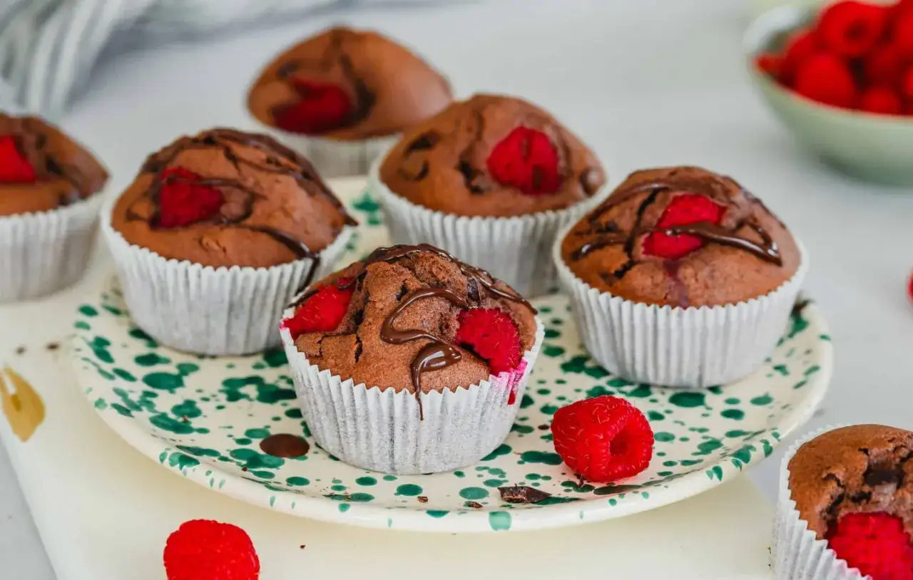 Saftige schokomuffins mit Himbeeren, verziert mit Schokoladenglasur, auf einem Teller mit gr&uuml;nen Tupfen.
