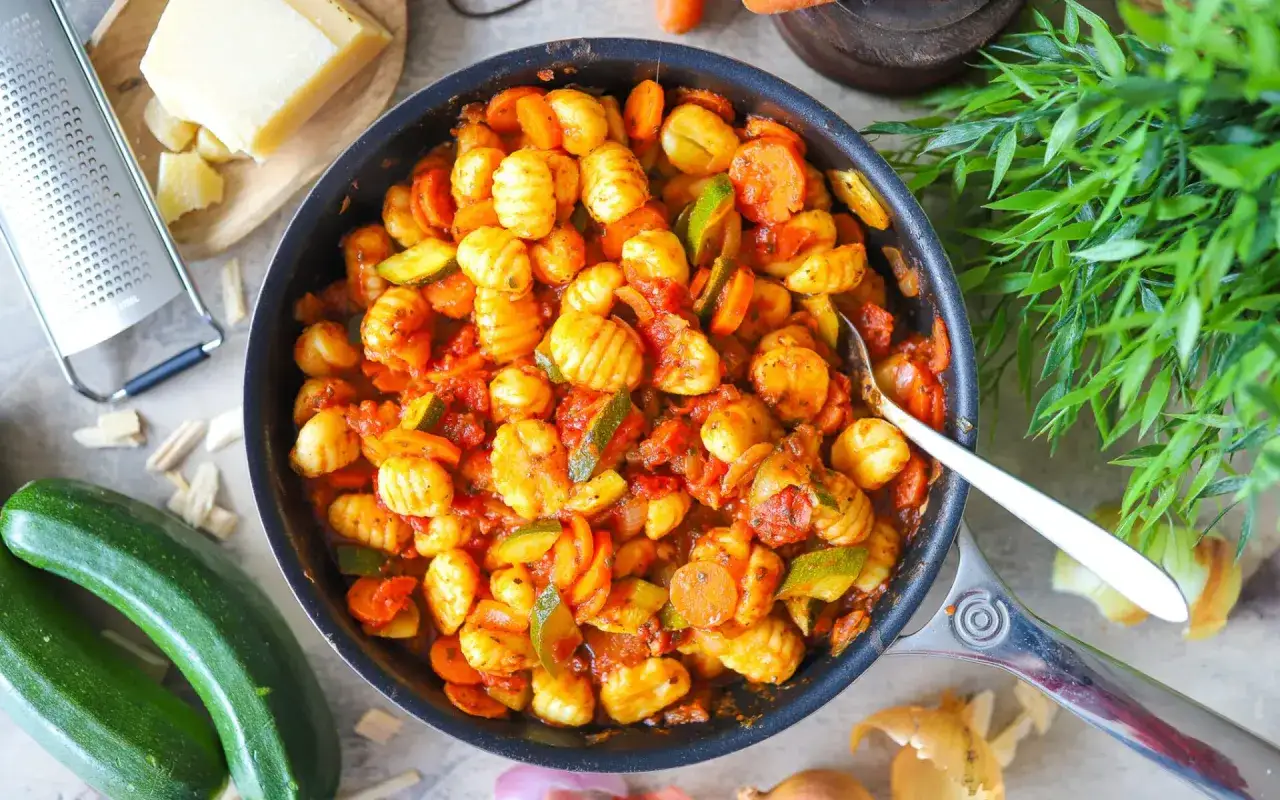 Herzhafte Gnocchi Rezepte mit Zucchini und Karotten in einer Tomatensauce, daneben frische Zutaten und Parmesan.