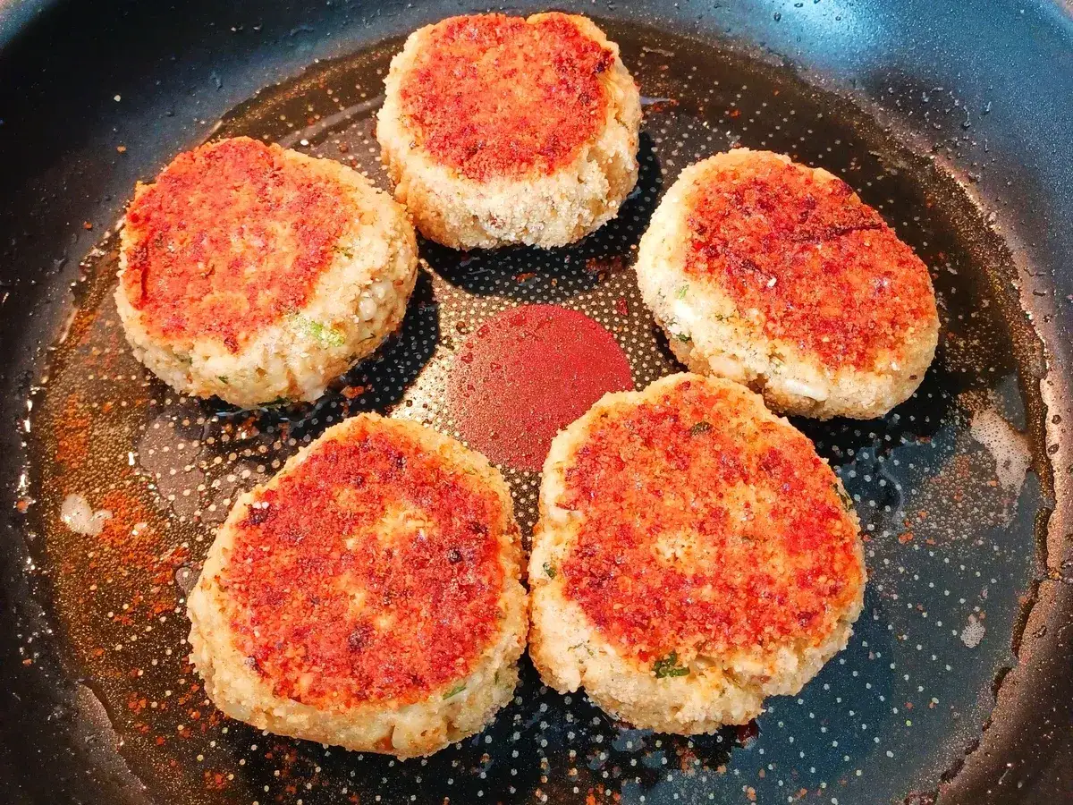 F&uuml;nf goldbraune vegetarische Frikadellen braten in einer Pfanne. Sie sind mit einer roten Kruste bedeckt und duften verlockend.