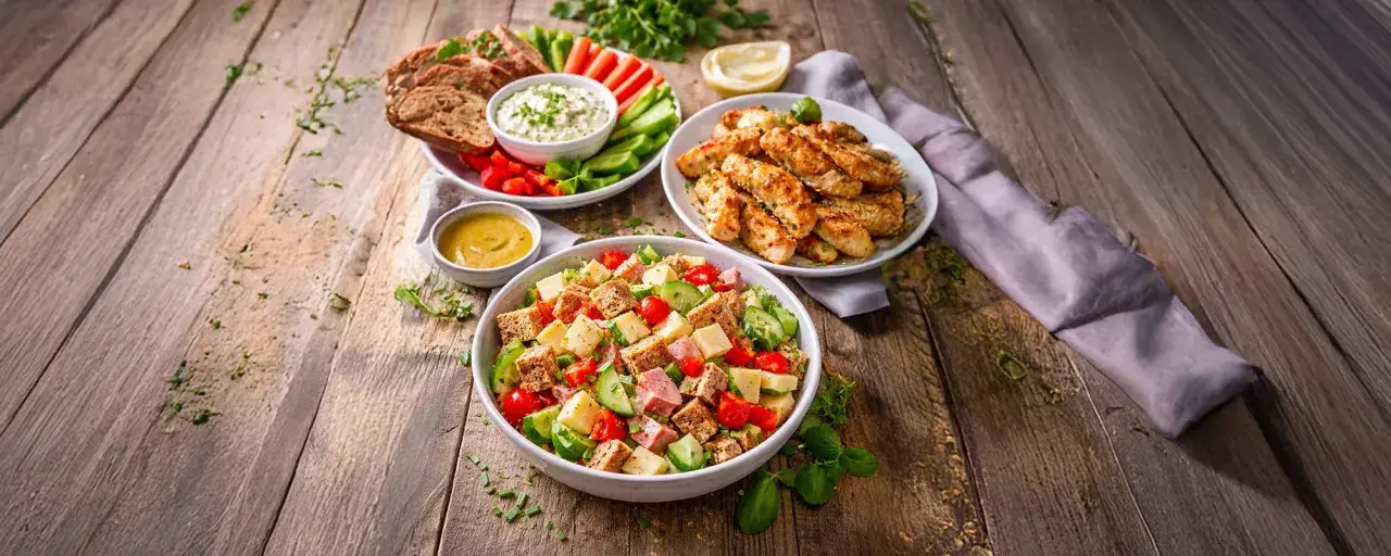 Leckere und schnelle Gerichte: bunter Salat, knuspriges Hähnchen und Brot mit Dip auf Holztisch.