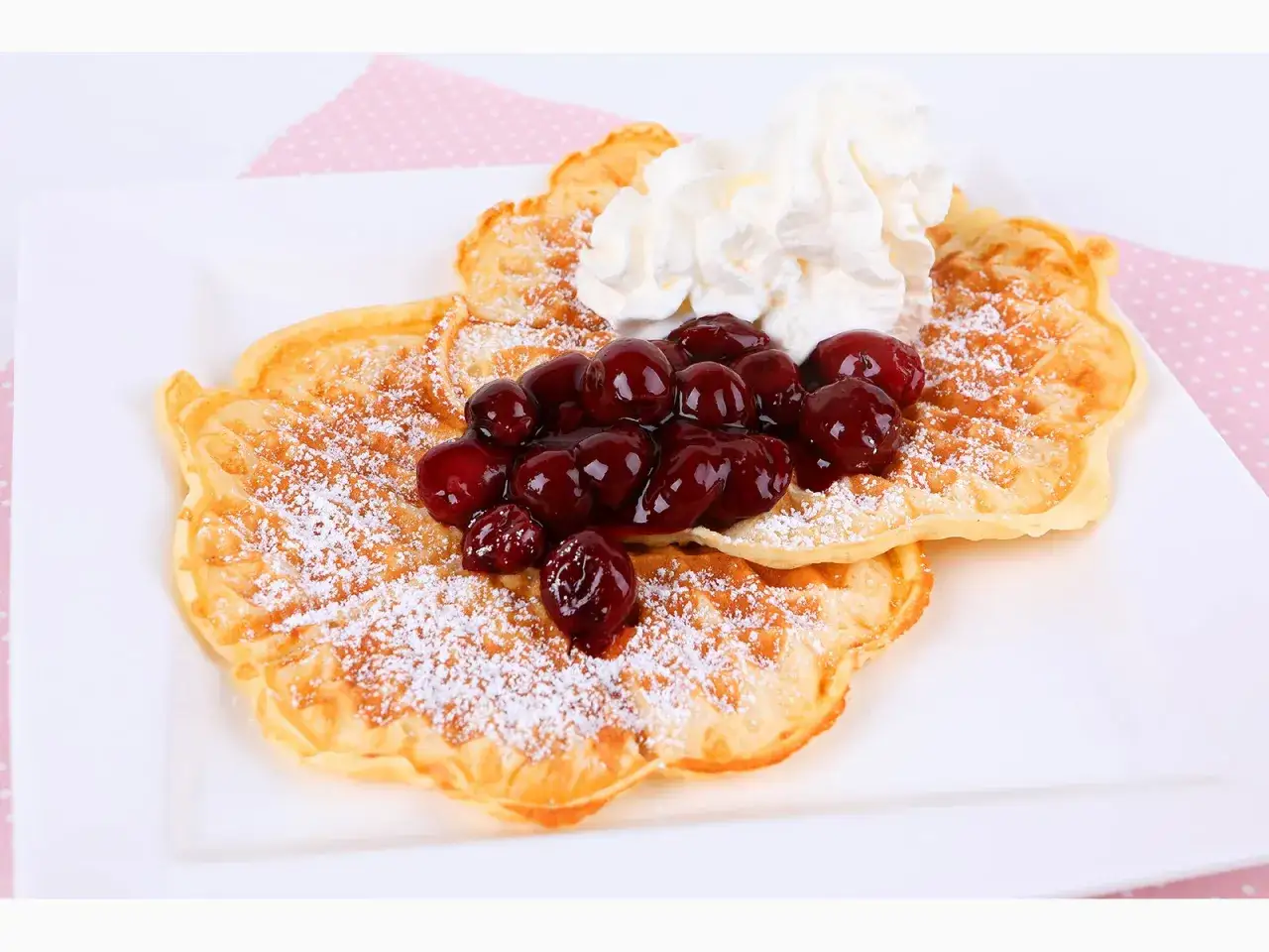 Zwei goldbraune Waffeln, bestäubt mit Puderzucker, belegt mit Kirschen und Sahne. Ein perfektes Waffeln Rezept für den Genuss.