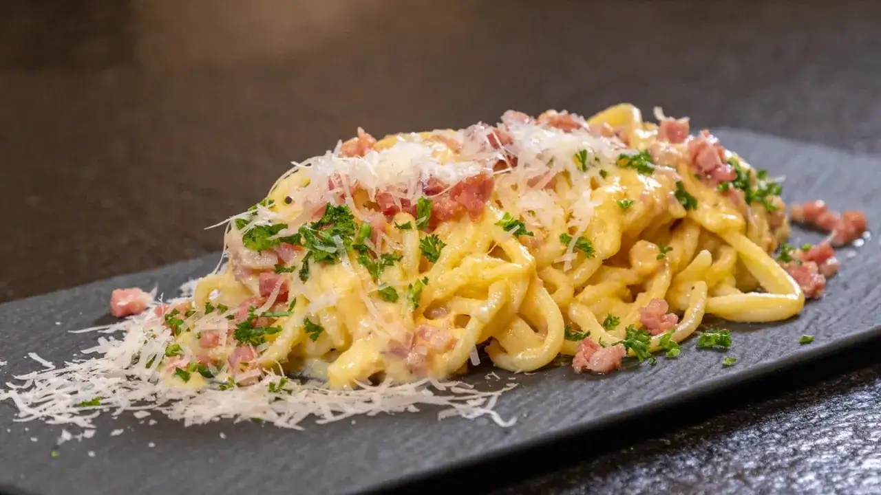 Ein Teller cremiger Spaghetti Carbonara, garniert mit Speckwürfeln, frischer Petersilie und geriebenem Parmesan.