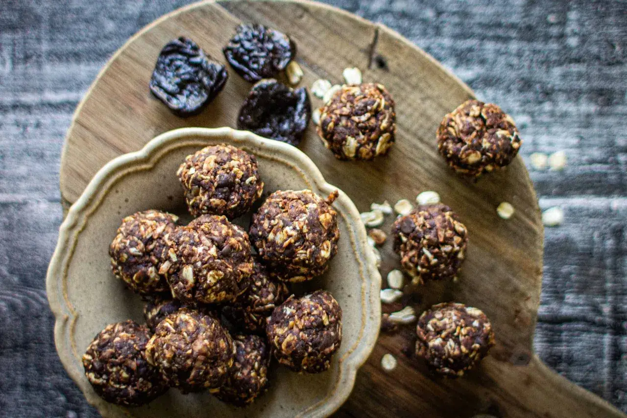 Schoko energy balls mit Haferflocken und N&uuml;ssen, daneben getrocknete Pflaumen. Ein gesunder Snack f&uuml;r zwischendurch.
