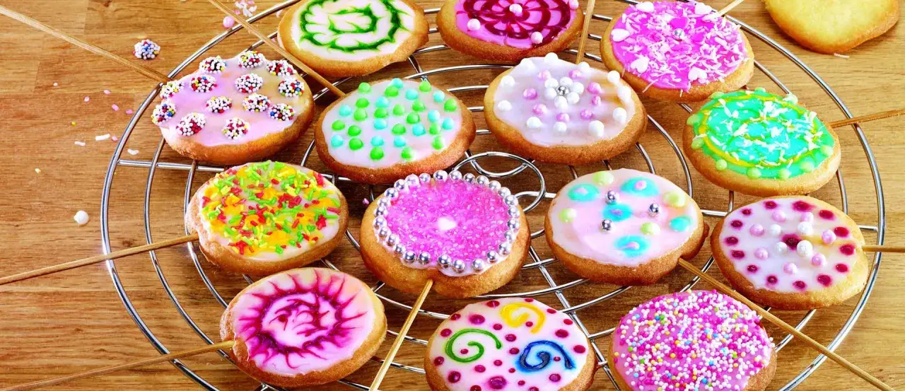 Bunte Kekse mit Zuckerguss mit Milch, verziert mit Streuseln und Perlen, auf einem Gitter.