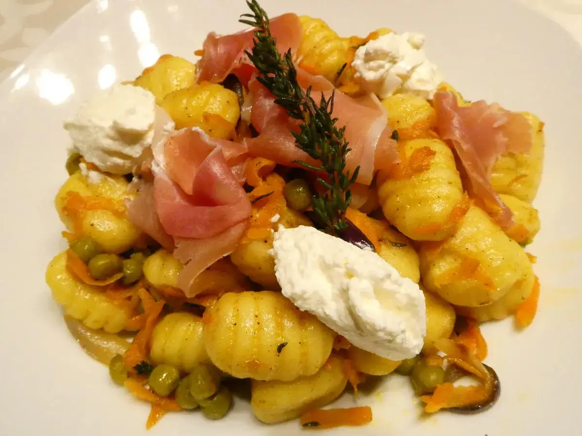 Gnocchi mit Speck, Erbsen und Karotten, garniert mit frischem Rosmarin und cremiger Ricotta.