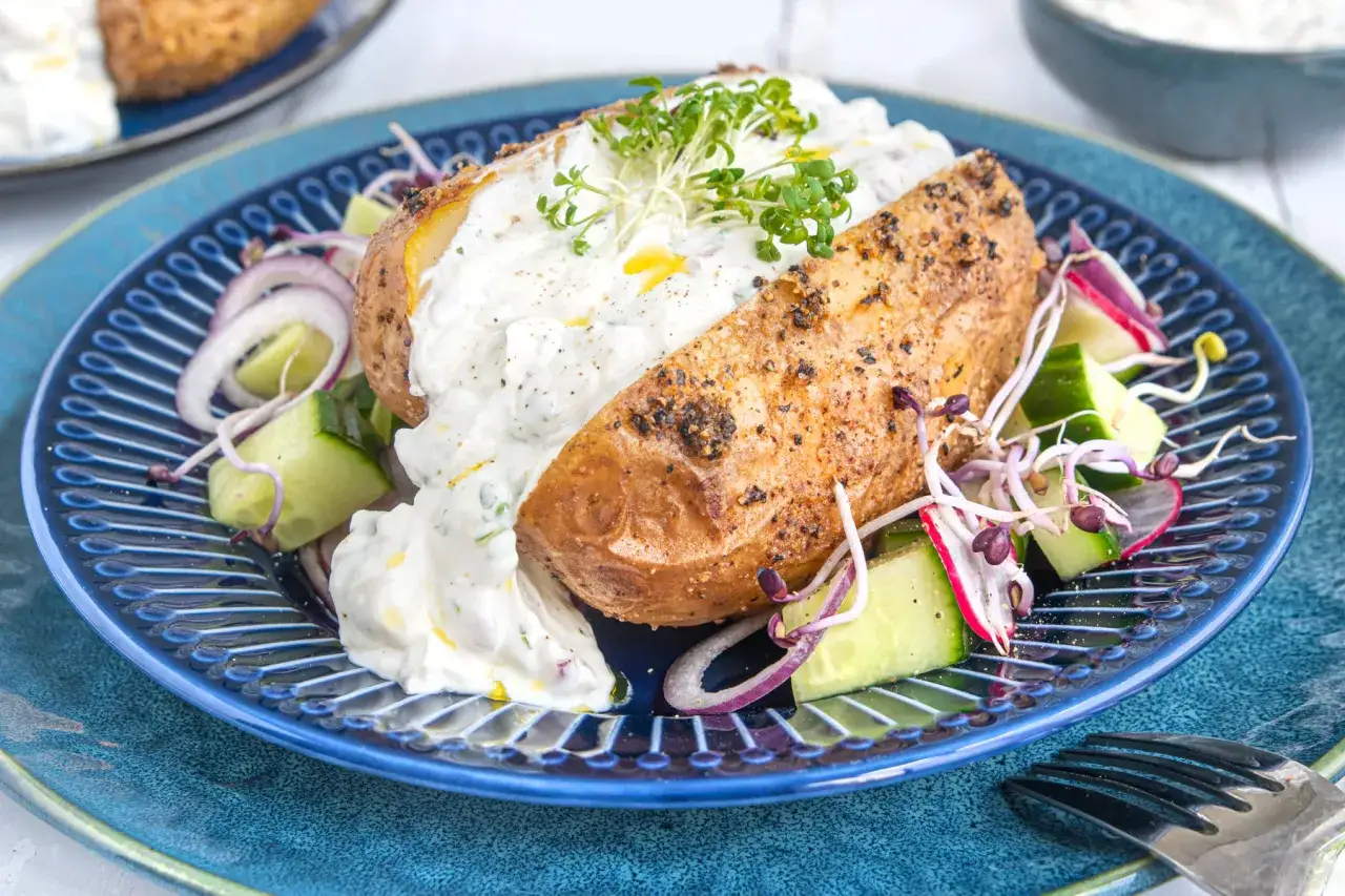 Ofenkartoffeln rezept: Eine gebackene Kartoffel mit Kräuterquark, Gurken, Radieschen und roten Zwiebeln auf einem blauen Teller.