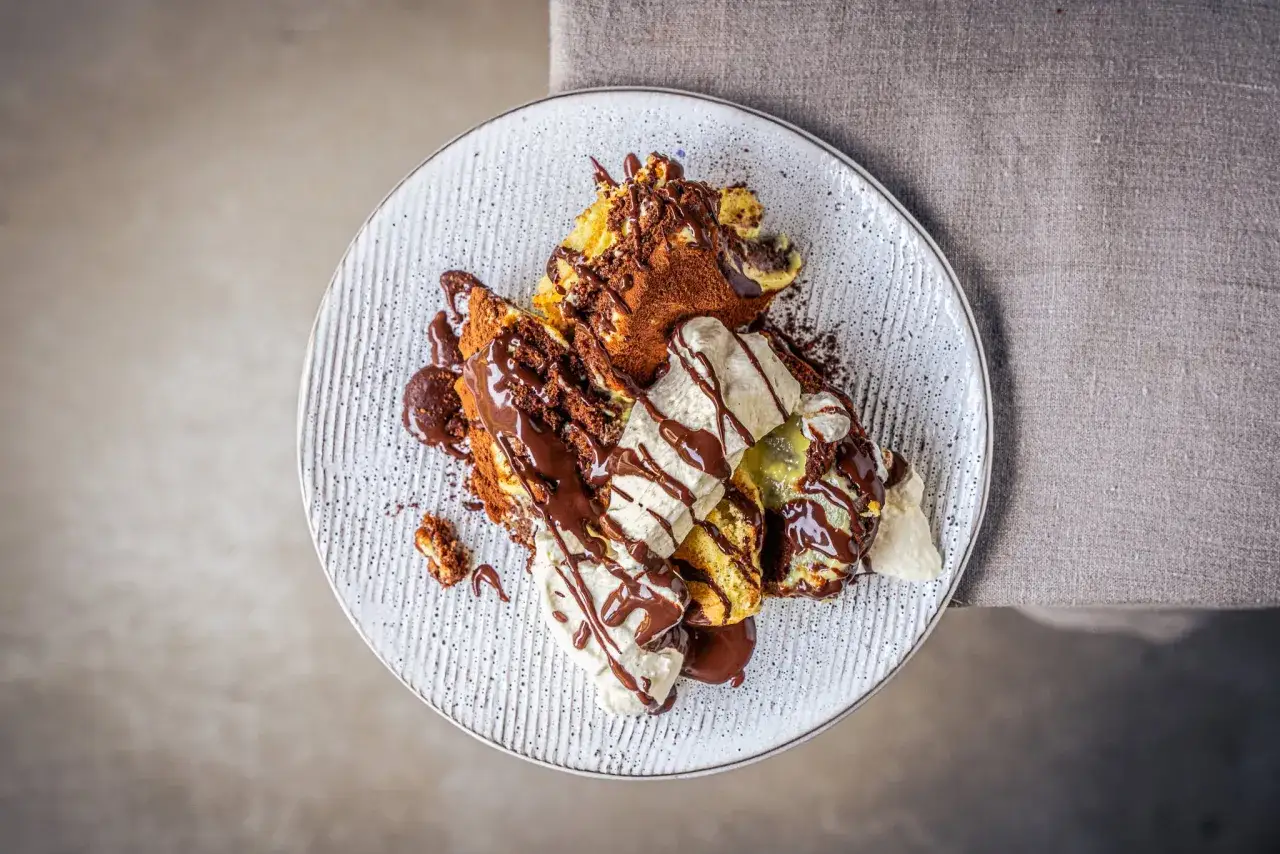 Ein k&ouml;stlicher Somlauer Nockerl-Dessert mit Schokoladensauce und Eiscreme, best&auml;ubt mit Kakaopulver.