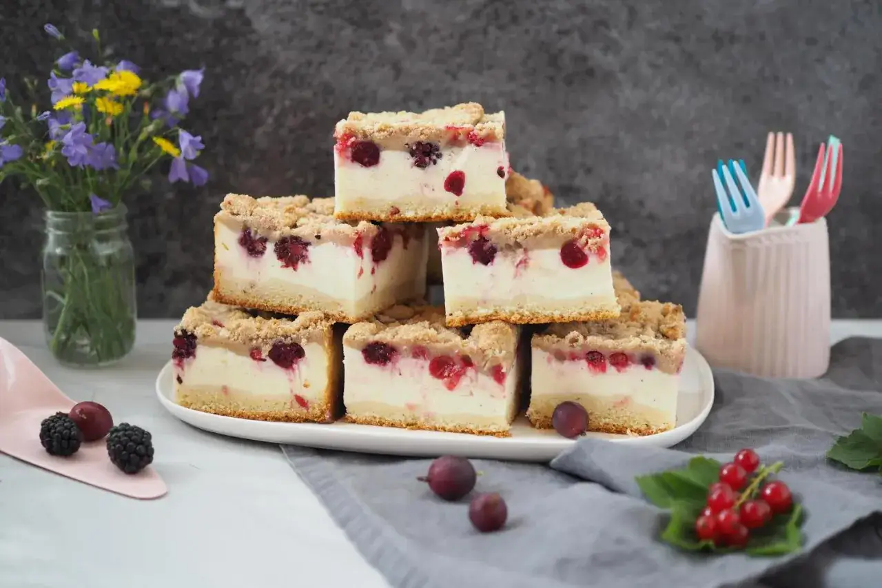 Saftiger Quarkkuchen ohne Boden mit roten Beeren und Streuseln, gestapelt auf einem Teller.