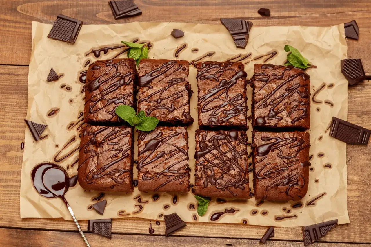 Saftiger Schokobiskuit vom Blech, dekoriert mit Schokoladenglasur und Minze. Schokoladenst&uuml;cke liegen verstreut.