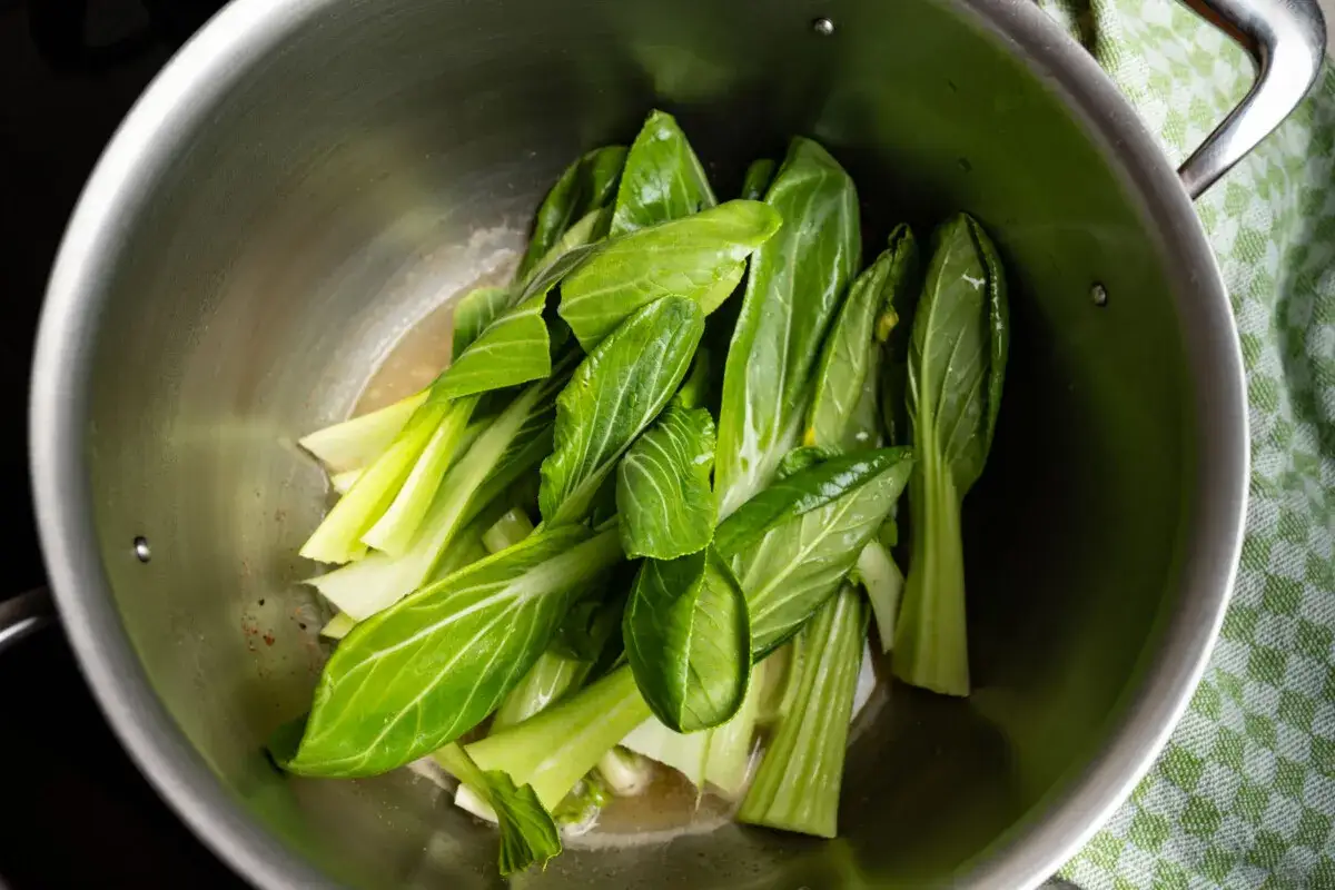Frischer Pak Choi wird in einem Topf mit etwas Flüssigkeit gedünstet.