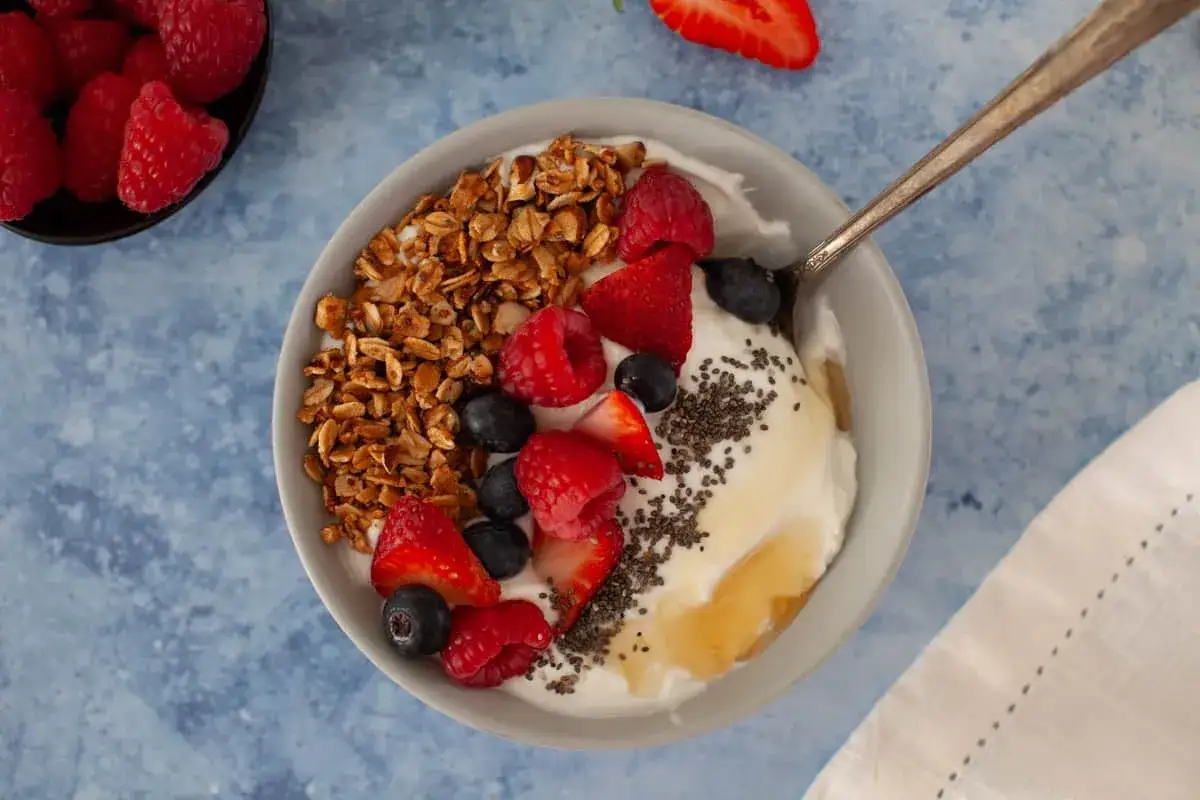 Sch&uuml;ssel mit Joghurt, Granola, Beeren und Honig. Leinsamen sind &uuml;ber den Joghurt gestreut.