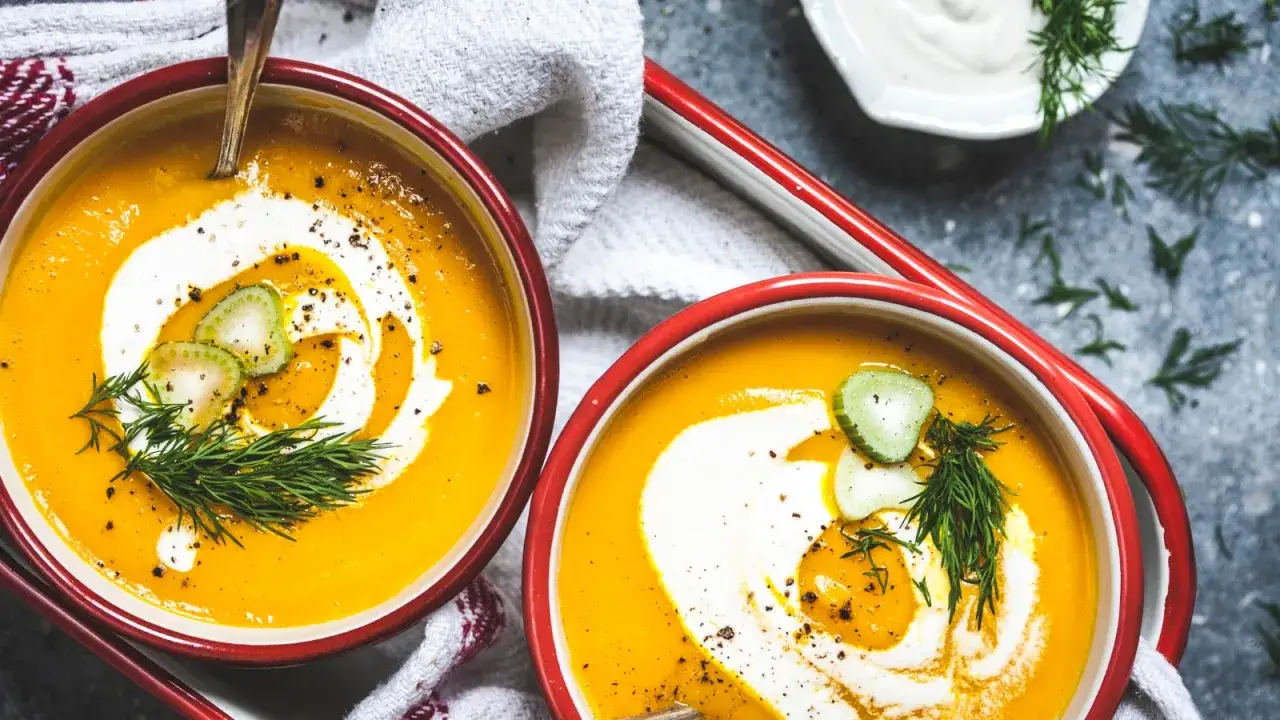 Zwei Sch&uuml;sseln cremiger K&uuml;rbissuppe, verziert mit einem Swirl aus Schlagsahne, Gurkenscheiben und Dill. Ja, man kann Schlagsahne zum Kochen nehmen, um Suppen zu verfeinern.