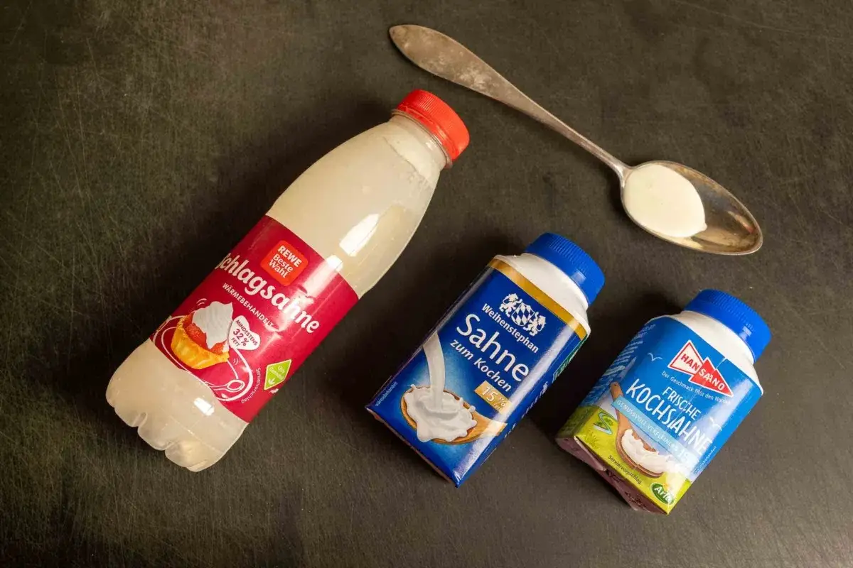 Drei Sahne-Packungen und ein L&ouml;ffel mit Sahne. Kann man Kochsahne schlagen? Die Packungen zeigen, dass es verschiedene Sorten gibt.