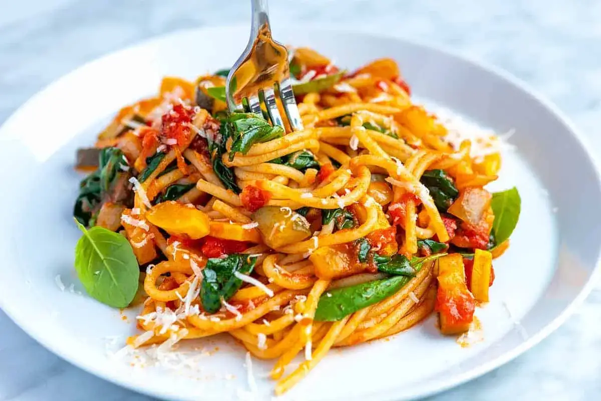Eine k&ouml;stliche, schnelle Nudelpfanne mit viel Gem&uuml;se und Parmesan. Ein Gabel hebt die Spaghetti an.