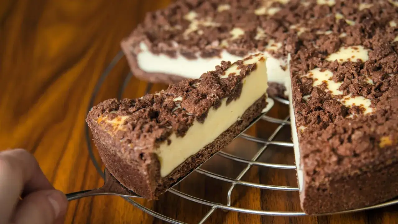 Ein Stück russischer Zupfkuchen wird aus dem Ganzen gehoben. Der Kuchen hat einen dunklen Boden, eine helle Füllung und eine Schokoladenstreusel-Decke.