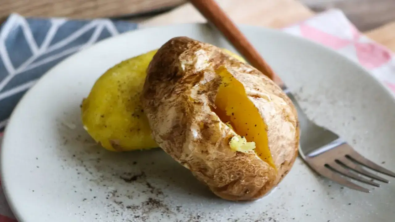 Zwei gebackene Kartoffeln, die in der Mikrowelle zubereitet wurden, liegen auf einem Teller. Eine Kartoffel ist aufgeschnitten und zeigt das weiche Innere.