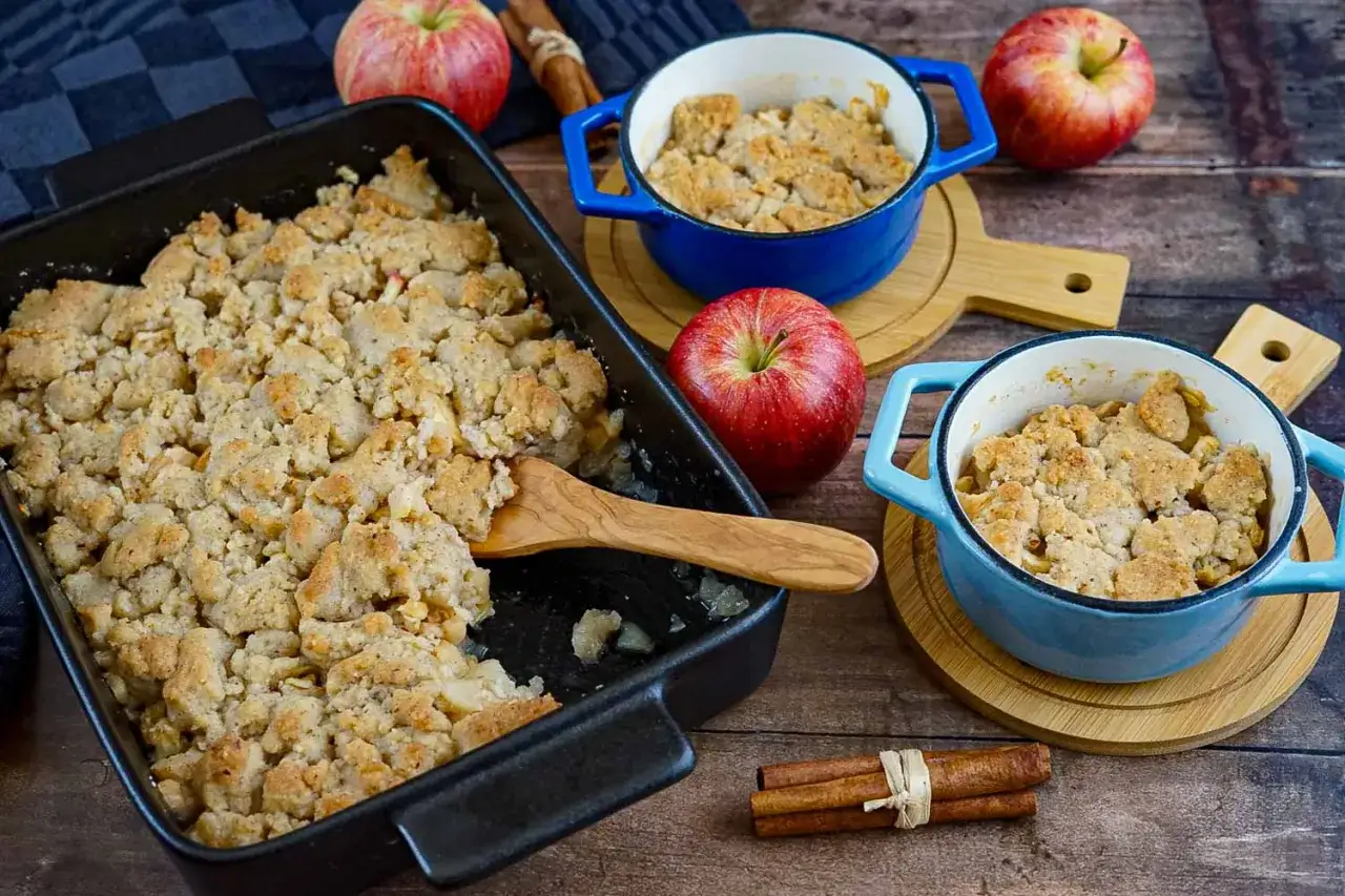 Leckerer Apfel-Crumble ohne Butter, goldbraun gebacken, daneben &Auml;pfel und Zimtstangen.