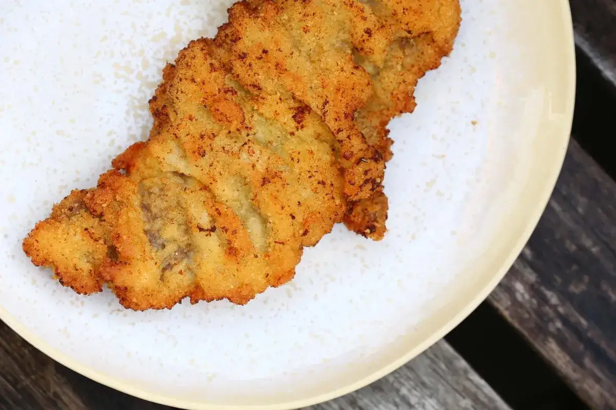 Ein goldbraunes Schnitzel, perfekt paniert, liegt auf einem Teller. Die knusprige Kruste zeigt, wie gut das Schnitzel paniert wurde.