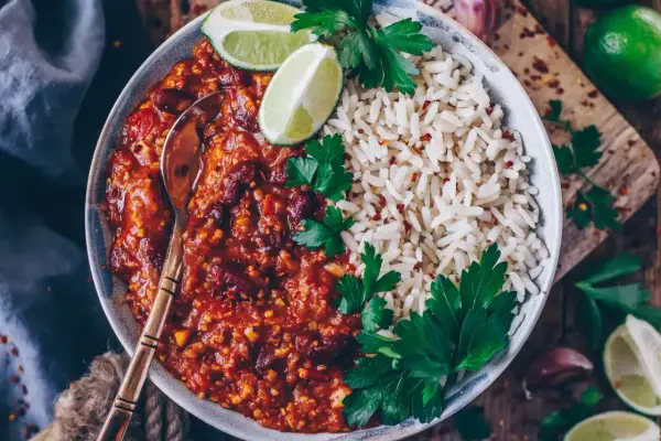 Herzhaftes Chili sin Carne mit Kidneybohnen, Reis, Limettenspalten und Petersilie. Ein Löffel wartet schon.