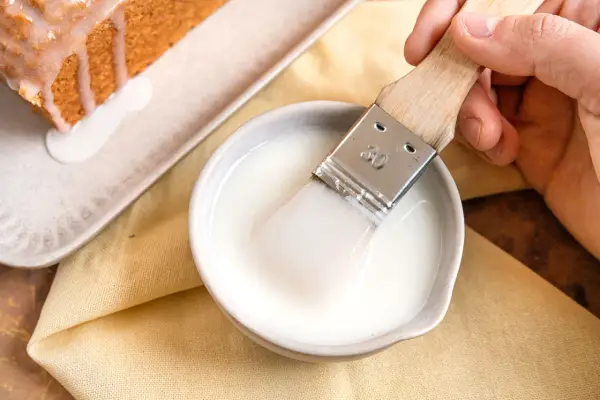 Ein Pinsel taucht in eine Schüssel mit zuckerguss, bereit, einen warmen oder kalten Kuchen zu verfeinern.