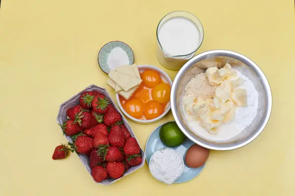 Zutaten für eine Erdbeerspiegel Torte: Erdbeeren, Eigelb, weiße Schokolade, Butter, Mehl, Zucker, Milch, Ei, Limette und Backpulver.